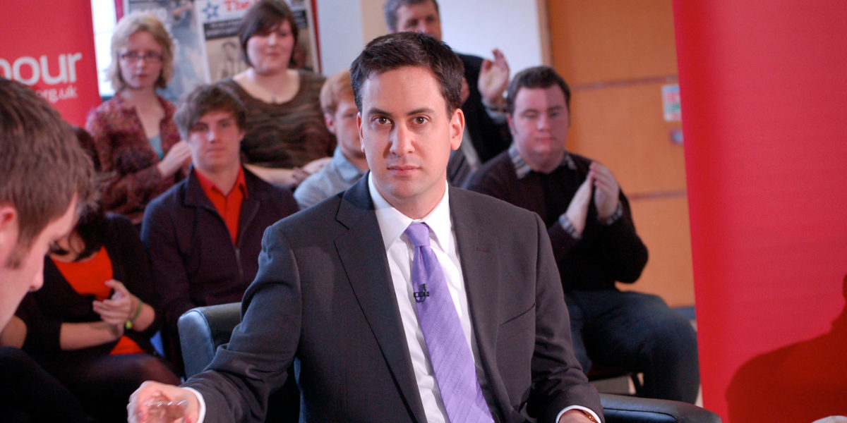 Former Labour party Ed Miliband at a public event facing the camera, with a group of young people behind him