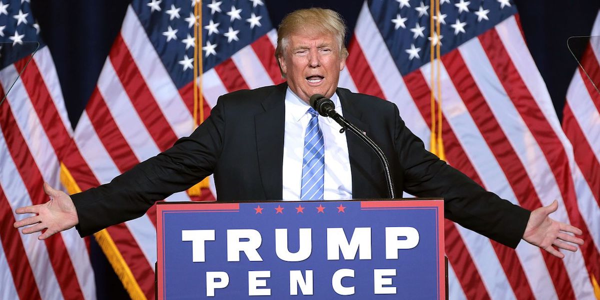 Donald Trump stands in from of US flags at a podium, arms spread wide, during a rally