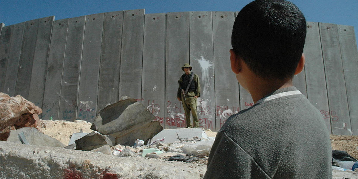 A young Palestinian boy faces an Israeli soldier along the West Bank border wall