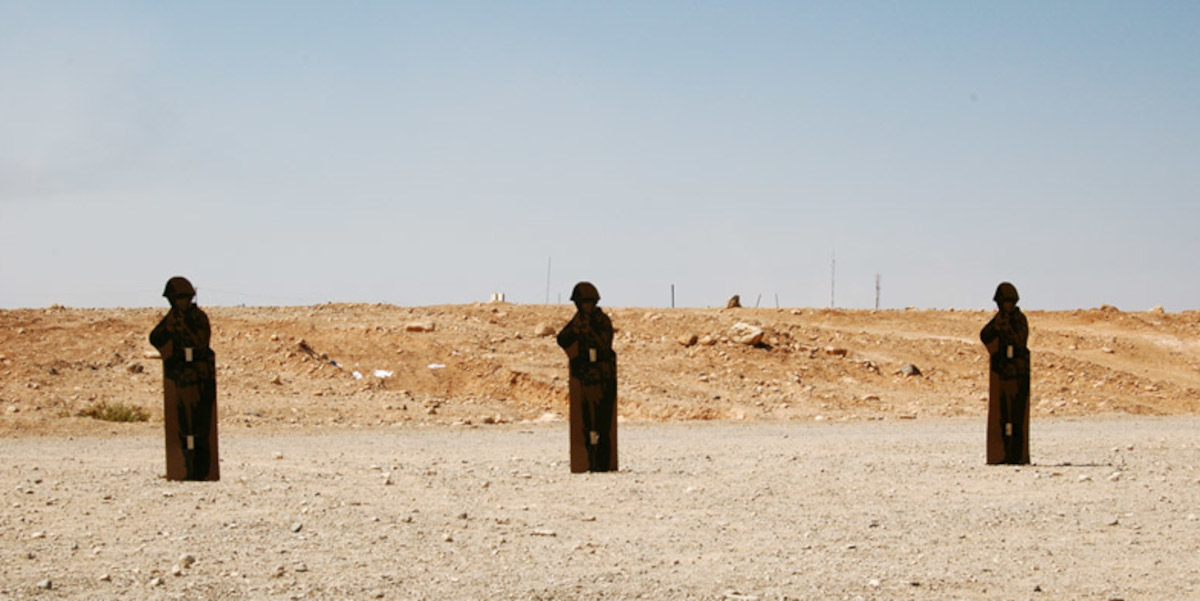 In a desert landscape stand three cardboard cutouts of soldiers