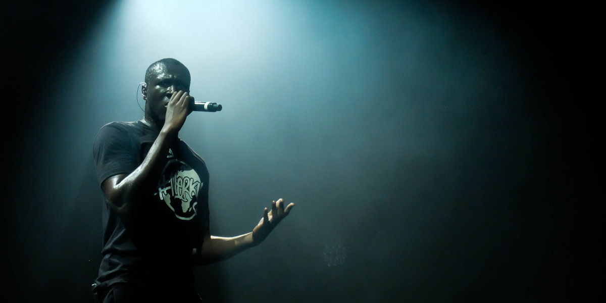 A Black man holding a microphone is bathed in stage lighting while he sings