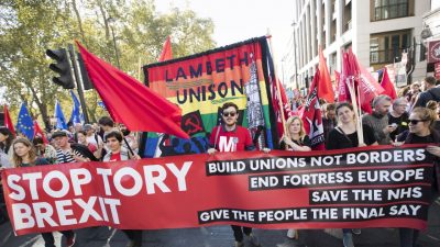 protestors march with red banner saying stop tory brexit