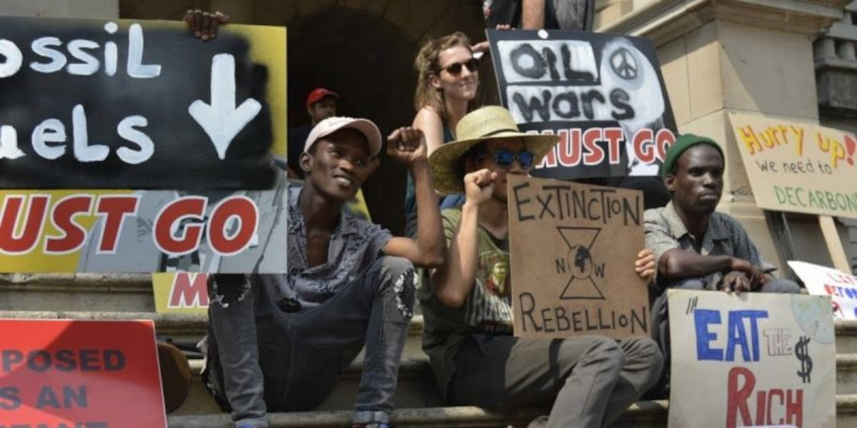 A group of multi-ethnic activists hold up placards for environmental justice and Extinction Rebellion