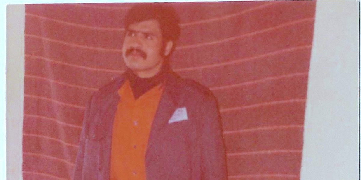 Ismail Abusalama, with a moustache, wears an orange shirt and stands against a striped background in prison