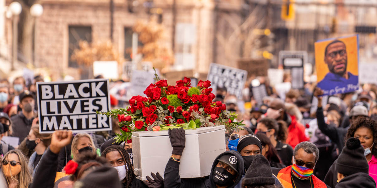 Protestors the day before Derek Chauvin's conviction, bearing a coffin as well as a portrait of George Floyd and a sign reading 'black lives matter'
