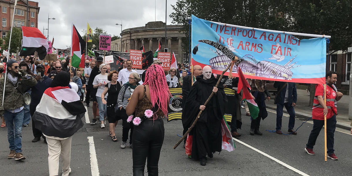 A protest march in central Liverpool featuring banners and a protestor in black robes holding a scythe