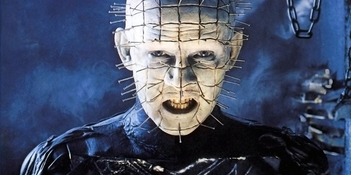 A monstrous male figure, bald, white faced, with long pins stuck into its entire head in a grid pattern