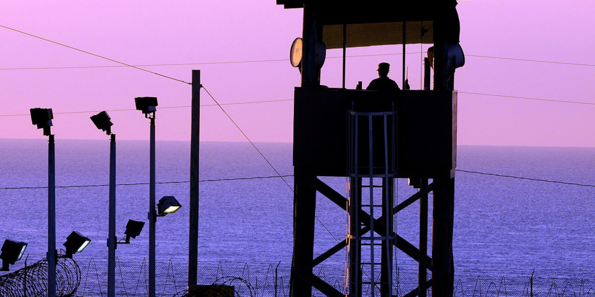 A guard in a watchtower at Guantanamo Bay looking over the sea at dusk