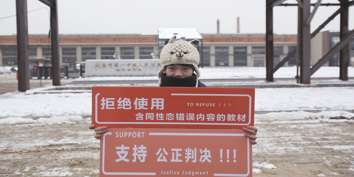 In a snowy scene, a person in a holly hats holds up signs in Chinese writing