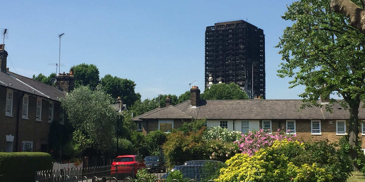 A leafy low-rise square with the burned remains of Grenfell Tower in the background