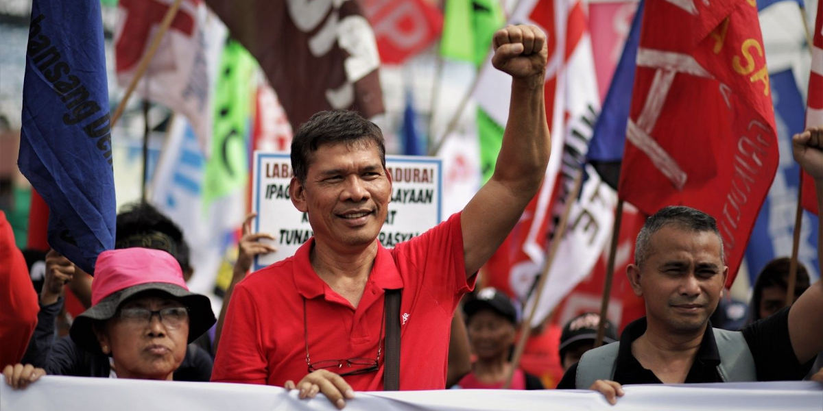 Philippine presidential candidate Leody de Guzman at a rally standing behind a banner with a raised fist