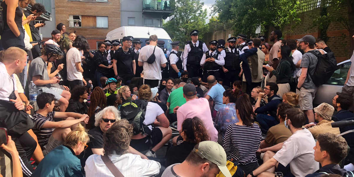 A crowd of people sat in front of a line of police officers attempting to conduct an immigration raid