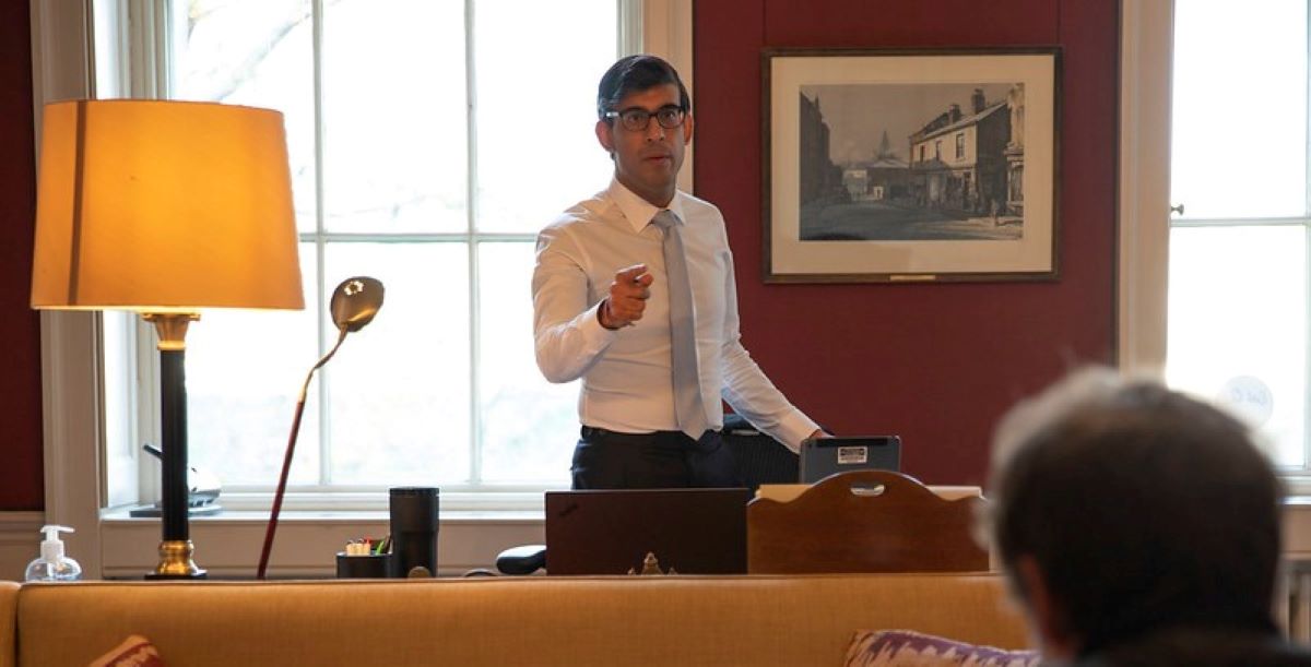 Rishi Sunak wearing a shirt and tie standing behind a desk