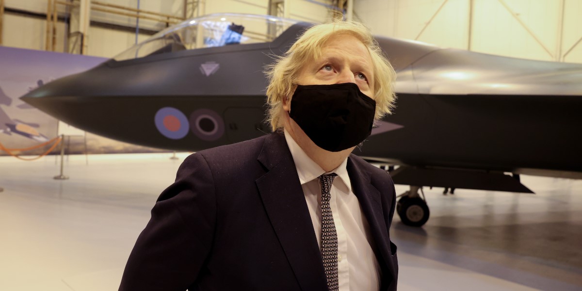 Boris Johnson wearing a black facemask standing in front of a fighter jet