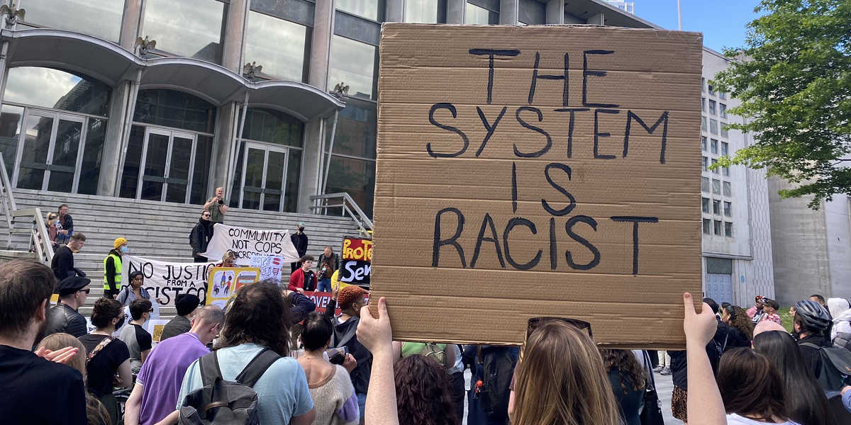 A woman holds up a sign reading: "The system is racist" at a protest outside court