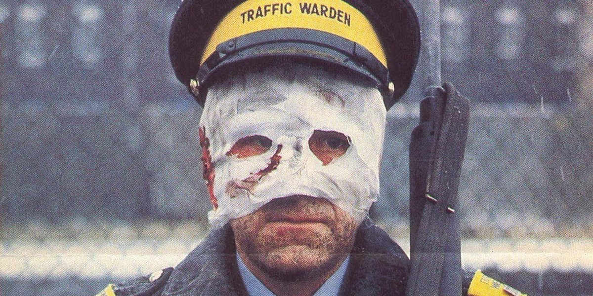 A man with a bandaged face and a traffic warden uniform standing guard with a rifle in a still from the 1984 film Threads