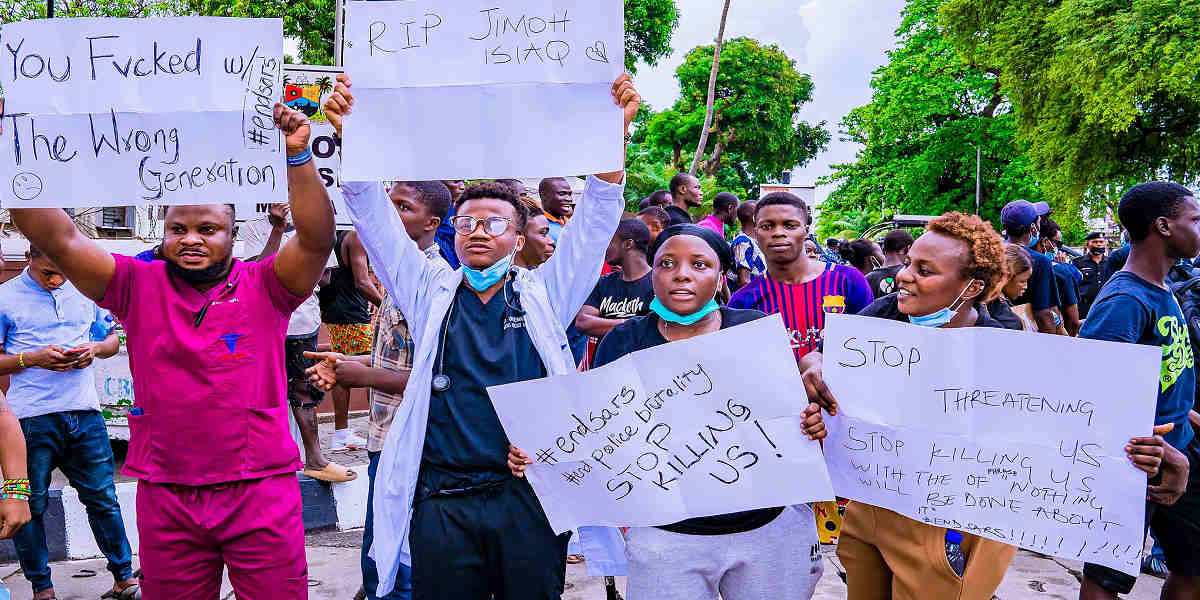Nigerian doctors in scrubs of various colours hold up placards demanding 'End SARS'