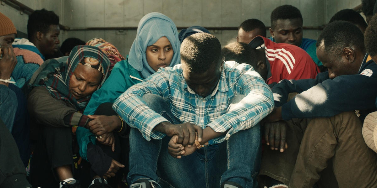 A group of people sitting on the floor, heads down, waiting