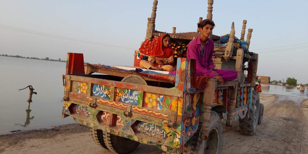 A boy in prink shirt and girl in orange head-scarf sitting on the back of a colourfully painted truck