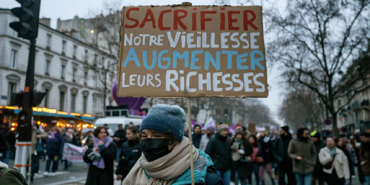A protestor in a face mask, scarf and woolly hat marches with a sign that reads 'sacrifice our old age, increase their wealth'