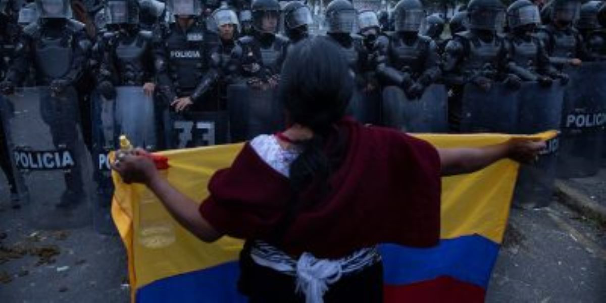 Protestor holding Ecuador flag, shown from the back, facing rows of police officers