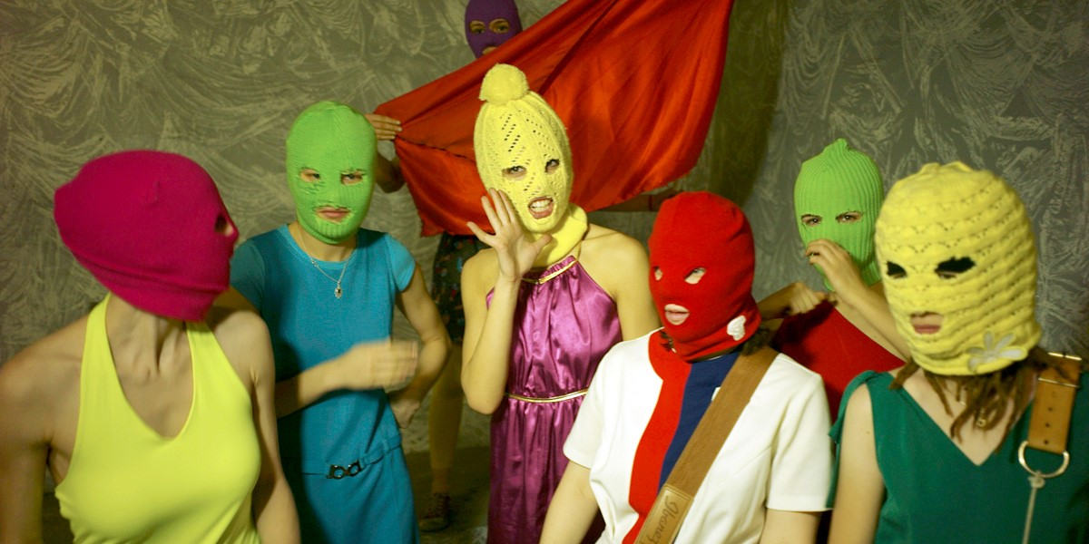 Six people pose in brightly coloured clothes and balaclavas