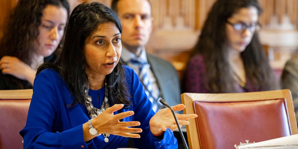 Suella Braverman wears a blue top and sits in a Lords committee room. She speaks into a microphone