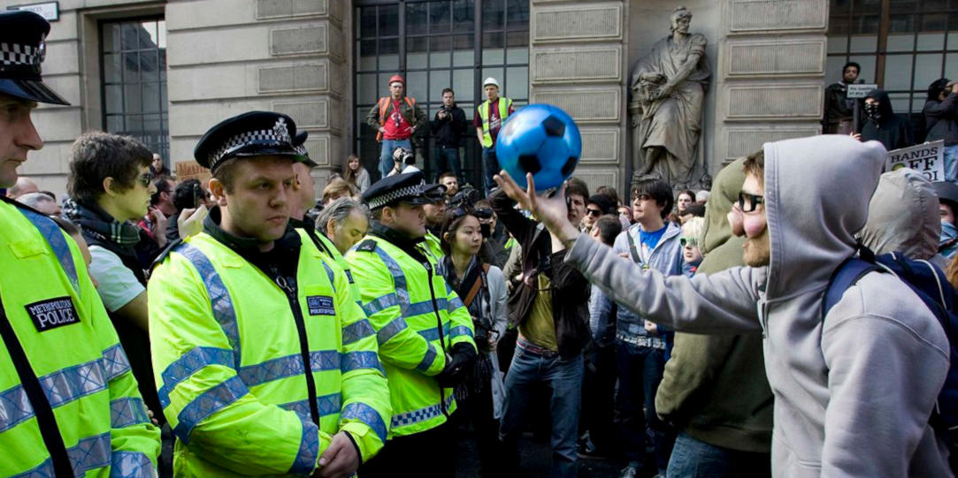A protestor wearing a pig nose confronts Metropolitan police officers wearing high vis jackets.