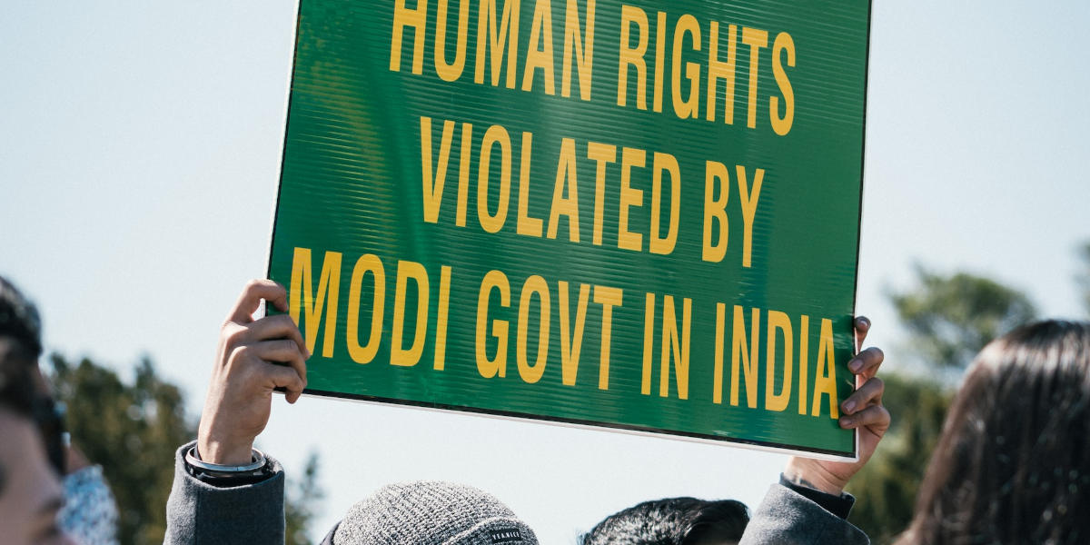 Someone holds up a green signed that says 'Human Rights violated by Modi govt in India' in yellow letters.