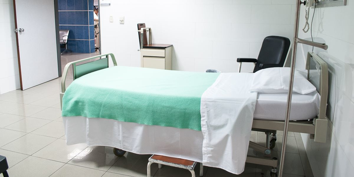 Bed in a hospital room with a chair and drawers by its side