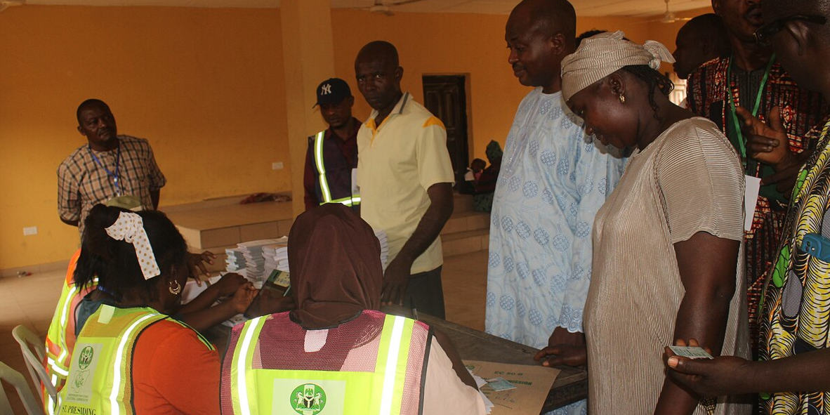A group of people attend a polling station in Nigeria. They are talking with election officials.