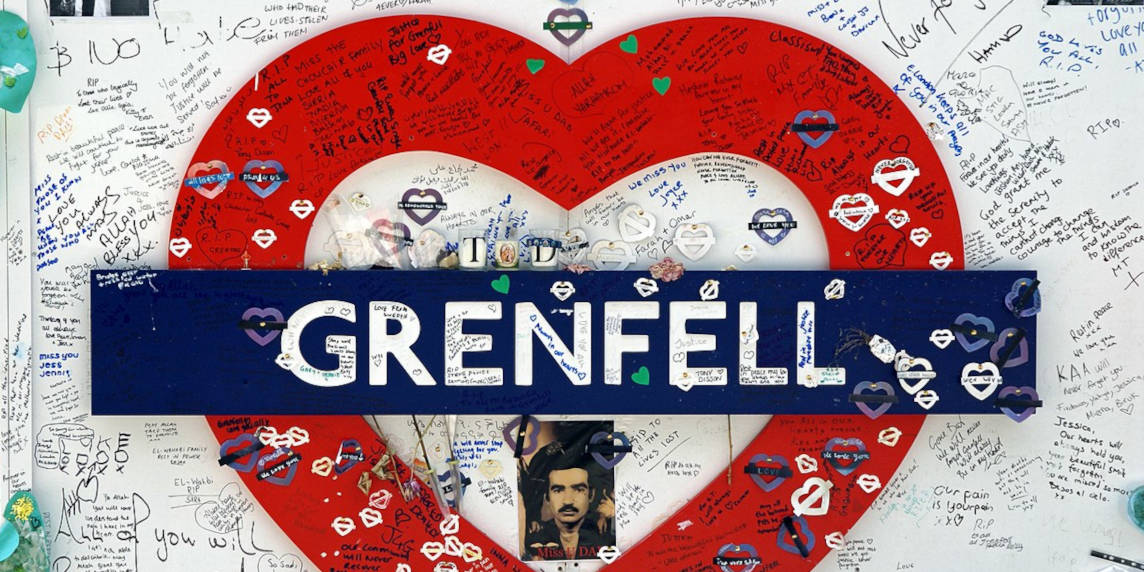A sign that says 'Grenfell' shaped like a heart. It is covered in people's hand written notes.