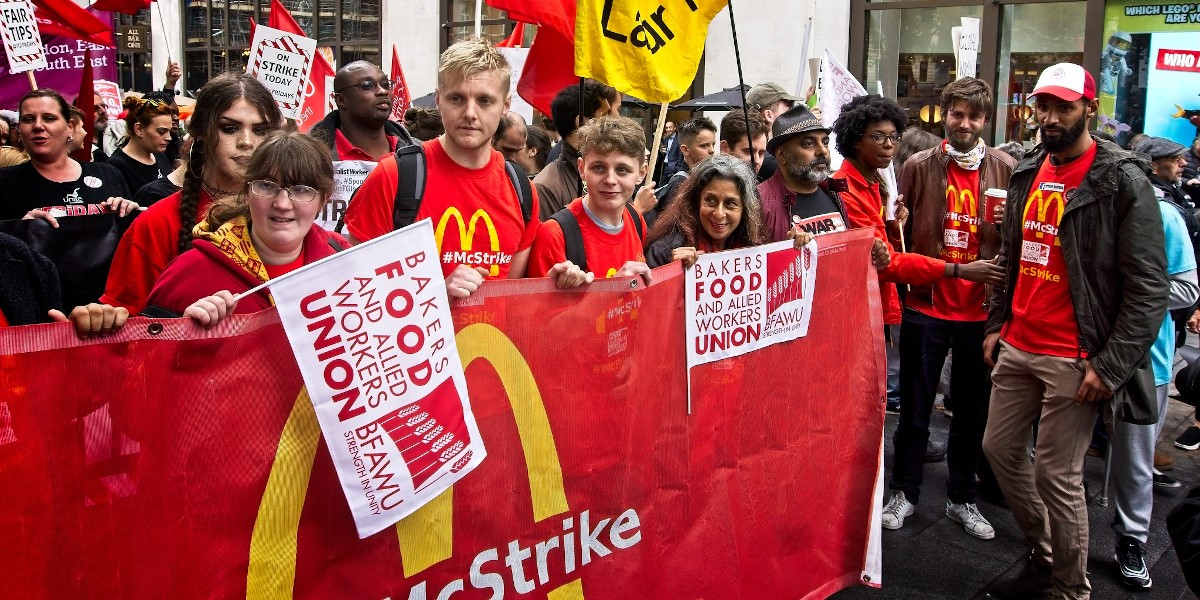 A rally of protesters march behind a large banner that reads: 'McStrike'