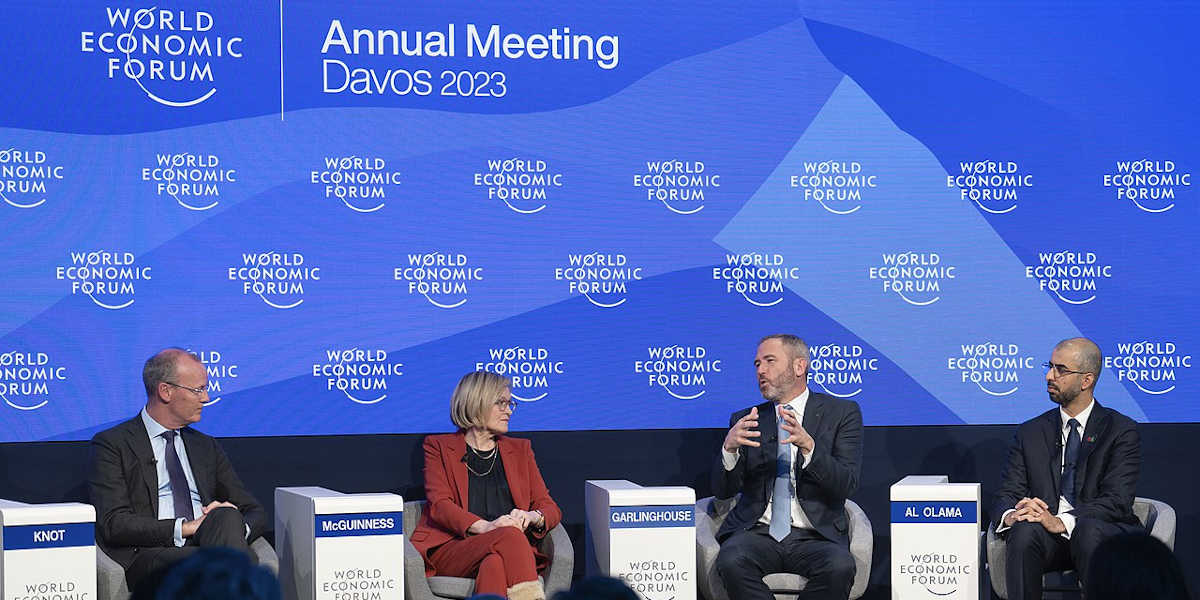 Four people in suits sit on a conference stage with a World Economic Forum branded backdrop