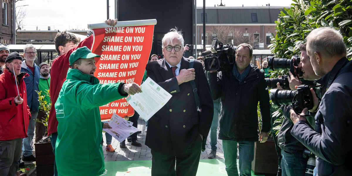 Protestor holds a red placard with 'Shame on you' written on it