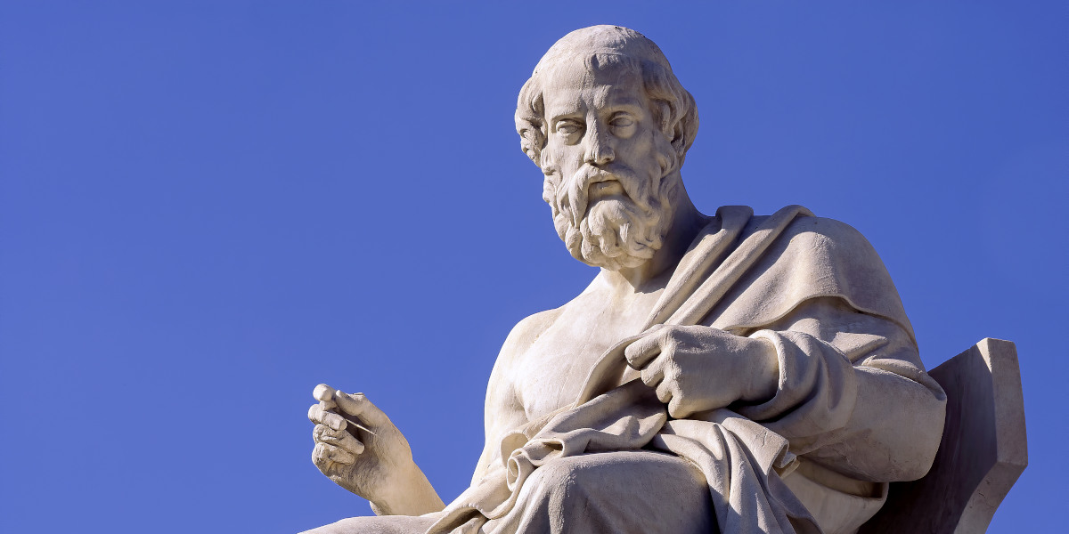 A marble statue of a bearded man, Plato, wearing a robe is offset against a bright blue sky