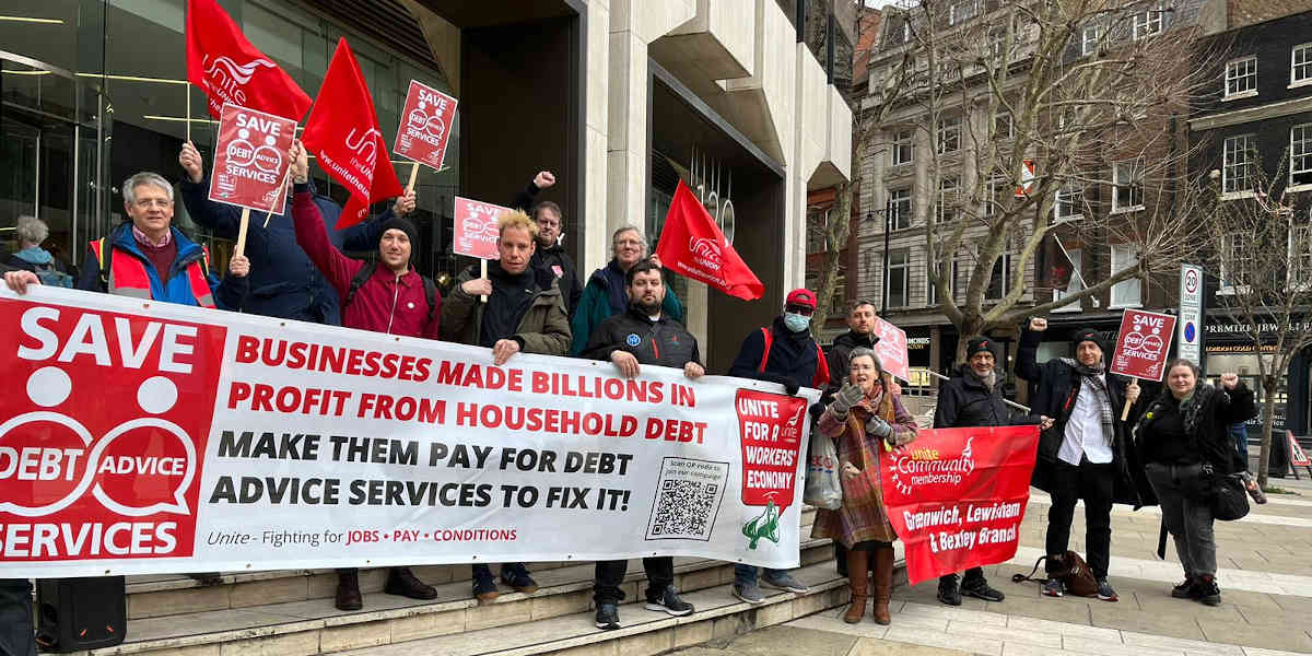 A dozen protesters stand of the steps of an office building waving Unison flags and holding placards and banners that read: 'Save Debt Advice' and condemning big business from profiting from household debt