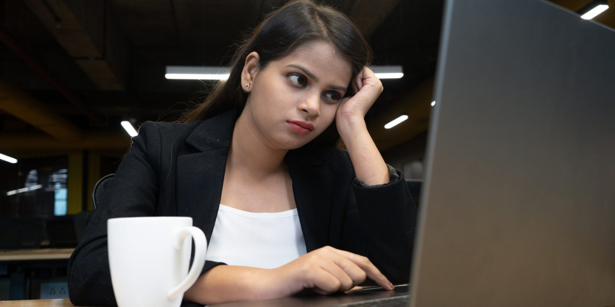 A young person, dressed for office work, looks despondently at a laptop computer