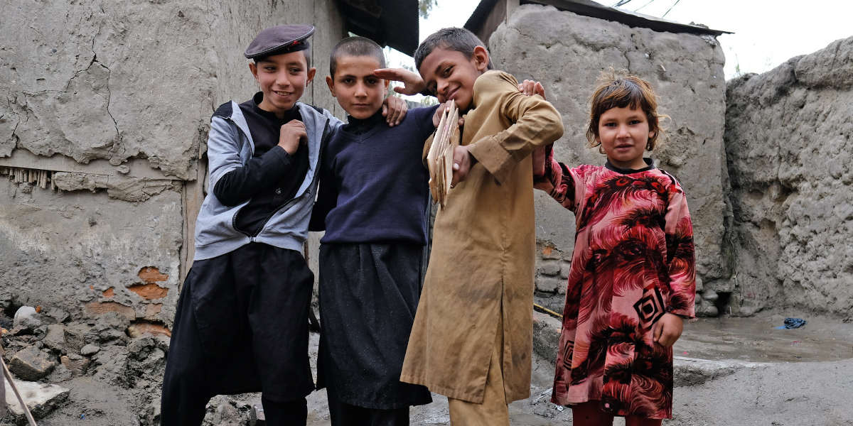 Four children are posing and looking at the camera against a backdrop of simple dwellings
