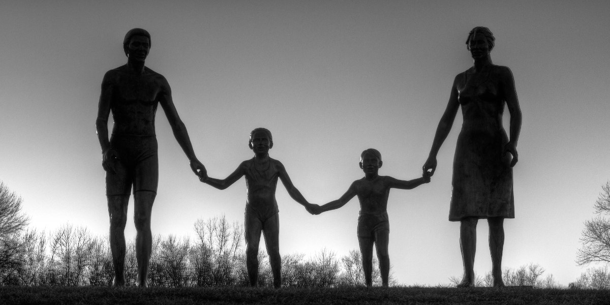 A black and white photo of a sculpture depicting a family of four holding hands, with both parents at either side