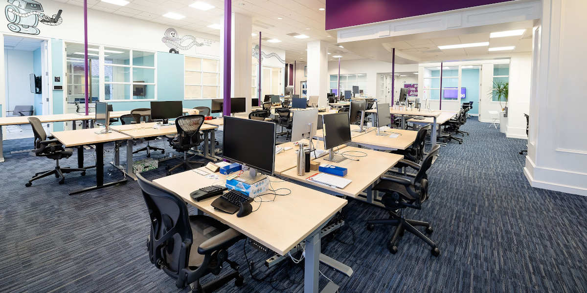 The interior of an office, showing several desks with computers on them