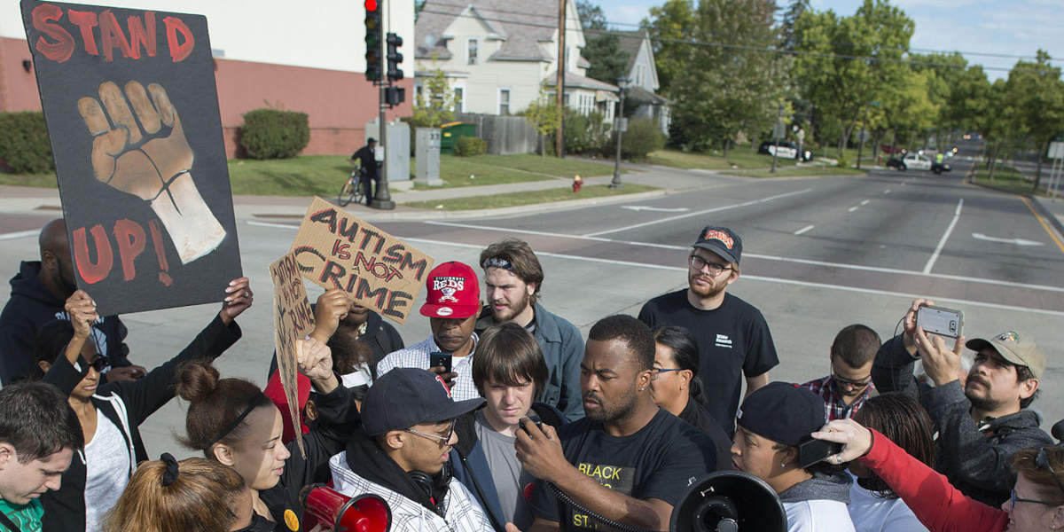 Protestors holding placards reading slogans including "stand up" and "autism is not a crime" blocking the the light rail line in St. Paul, Minnesota