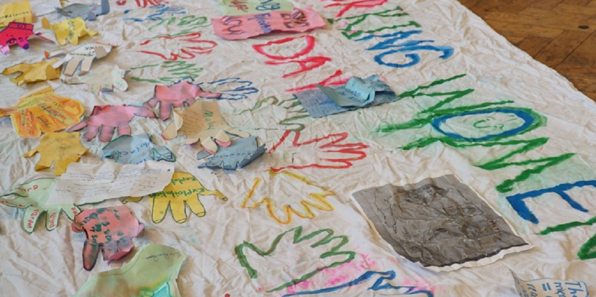 A banner is on the floor, it is covered in colourful hand prints containing illegible text.