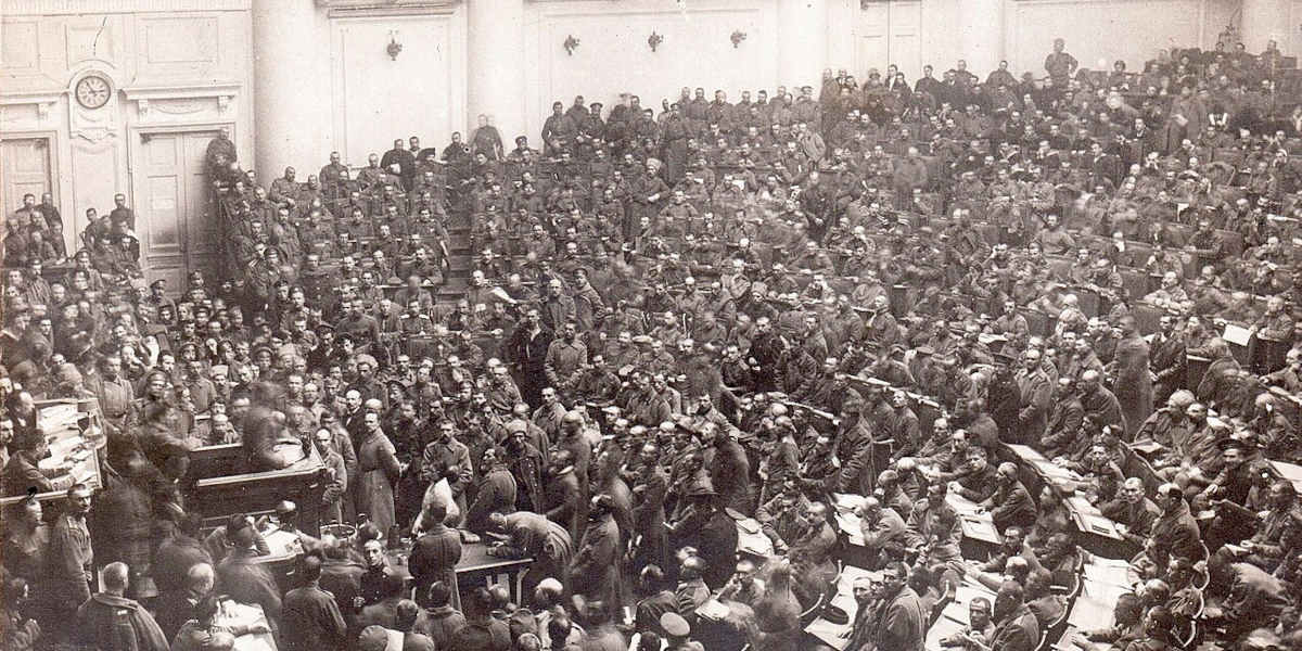 A black and white photograph showing the Petrograd Soviet in session, with crowds of delegates in a busy, semi-circular chamber taken from above