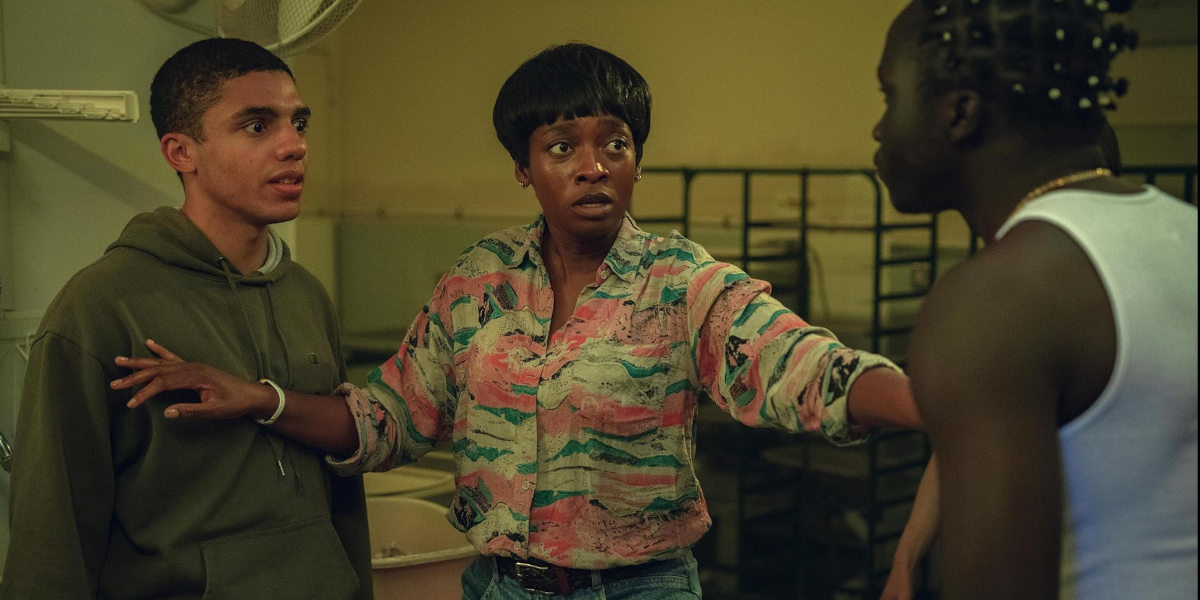 A woman stands between two men, seeming to stop them from fighting