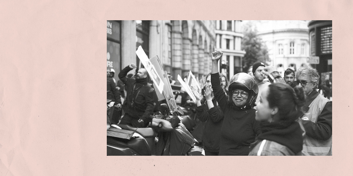 A b&w photo of a protester with a bike helmet, fist raised in the air
