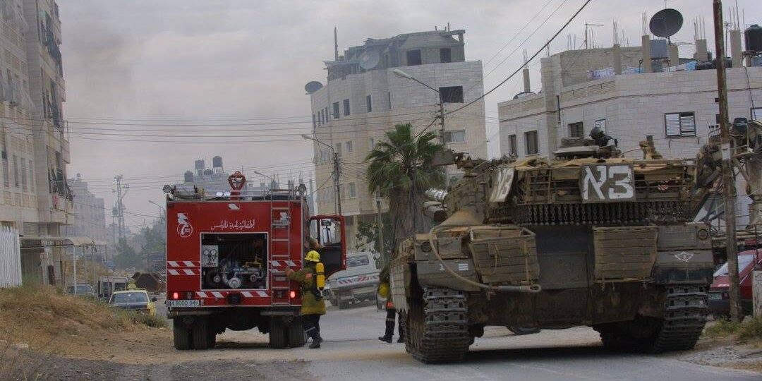 This image depicts a Palestinian fire truck next to an Israeli Defence Forces (IDF) armoured vehicle