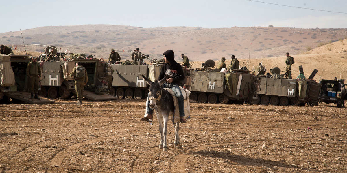 A Palestinian boy on a donkey looks at Israeli military vehicles, during a large scale military training in the northern Jordan Valley, West Bank