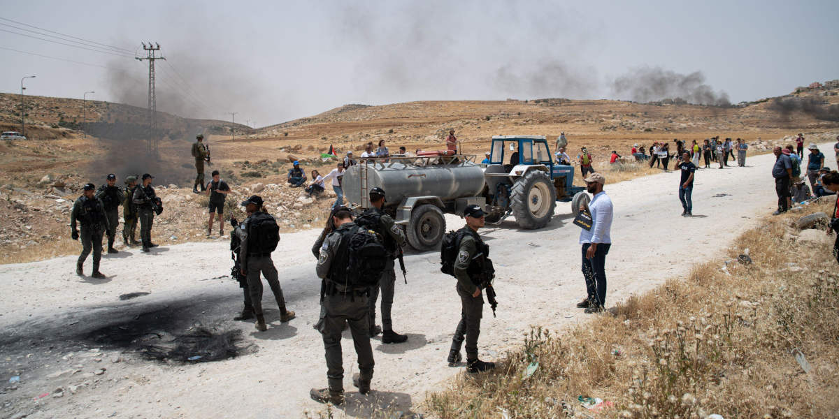 Protestors on either side of a road allowing a tractor to drive through