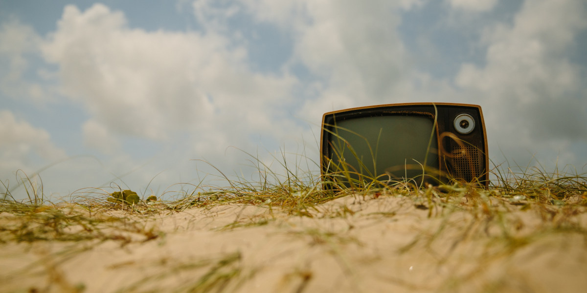 A stock photo of an old Television resting on sandy ground